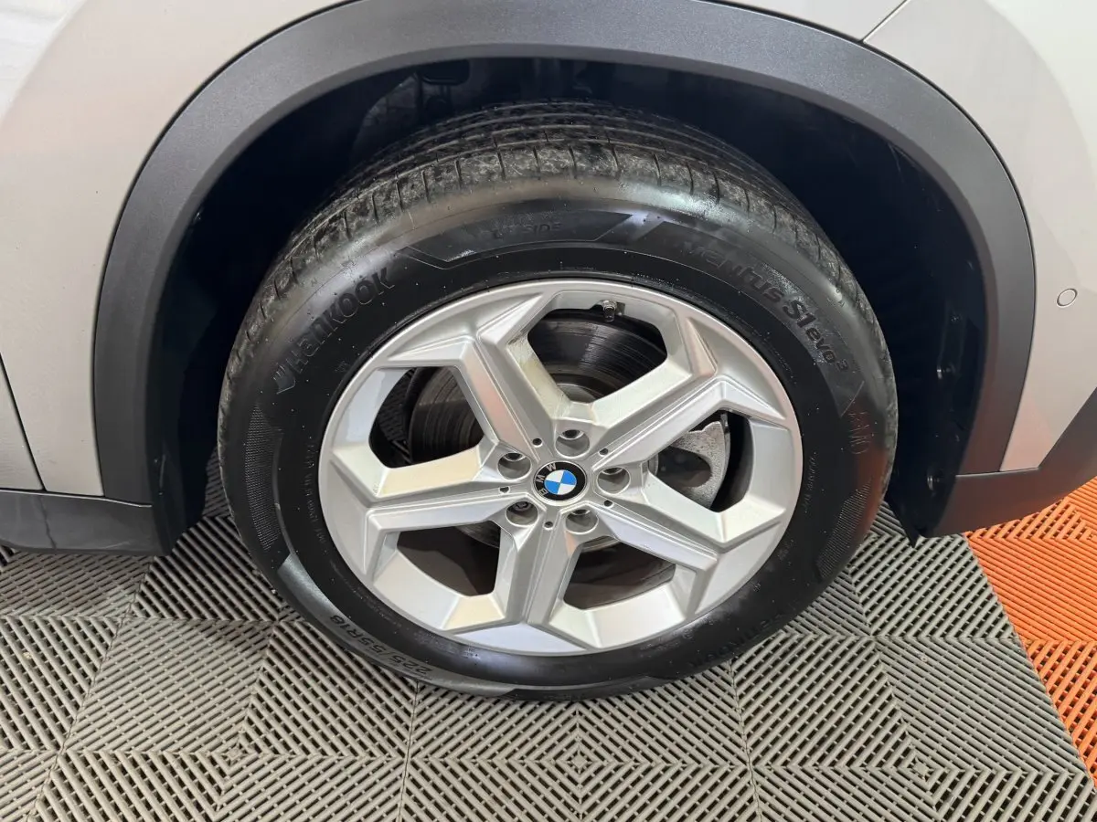 Gros plan sur la roue avant droite d’un BMW X1 gris foncé, avec jante alliage et passage de roue noir.