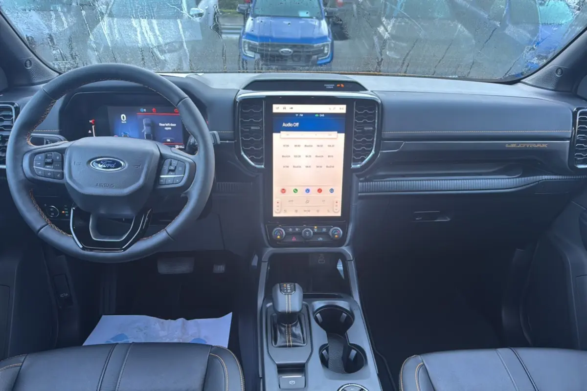 Vue intérieure avant du Ford Ranger Wildtrak 2026, tableau de bord noir avec écran tactile vertical et volant cuir multifonctions.
