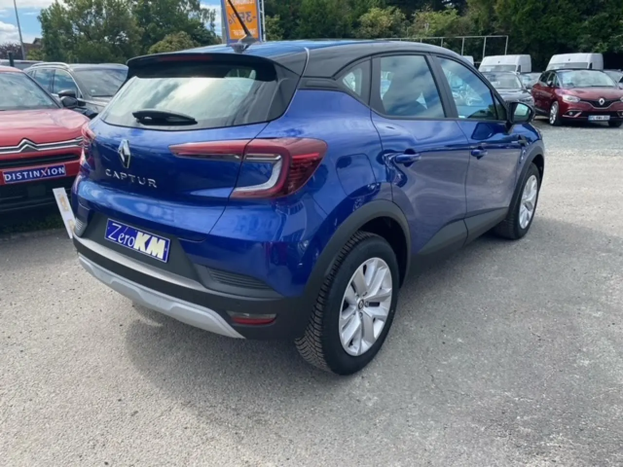 Vue 3/4 arrière droite d'un Renault Captur bleu Iron 2023 avec toit noir et jantes argentées sur parking.