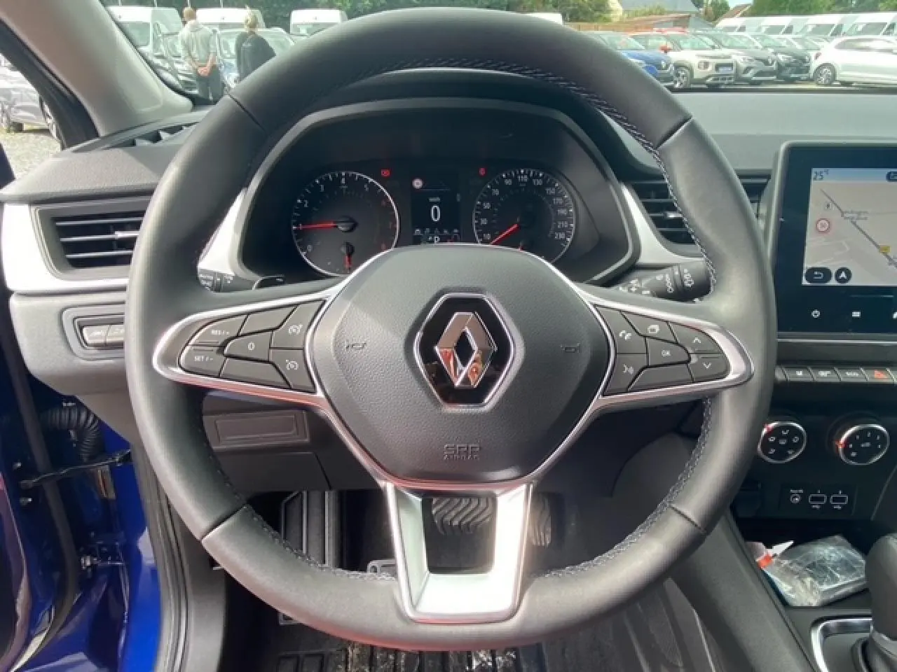 Vue intérieure centrée sur le volant du Renault Captur bleu 2023 avec tableau de bord et écran de navigation visible.
