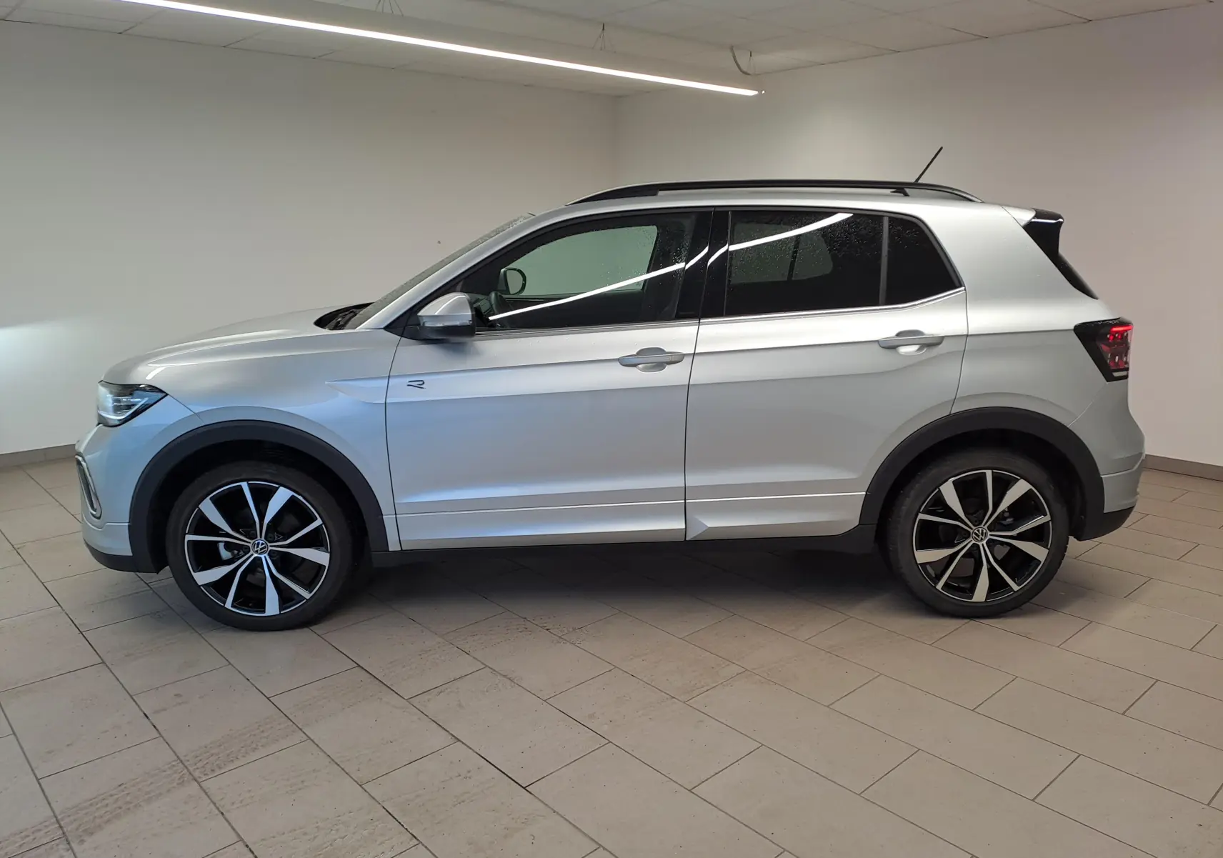 Vue de profil côté gauche d'un Volkswagen T-Cross 2025 argent Reflet, version R-Line avec jantes noires et argentées.