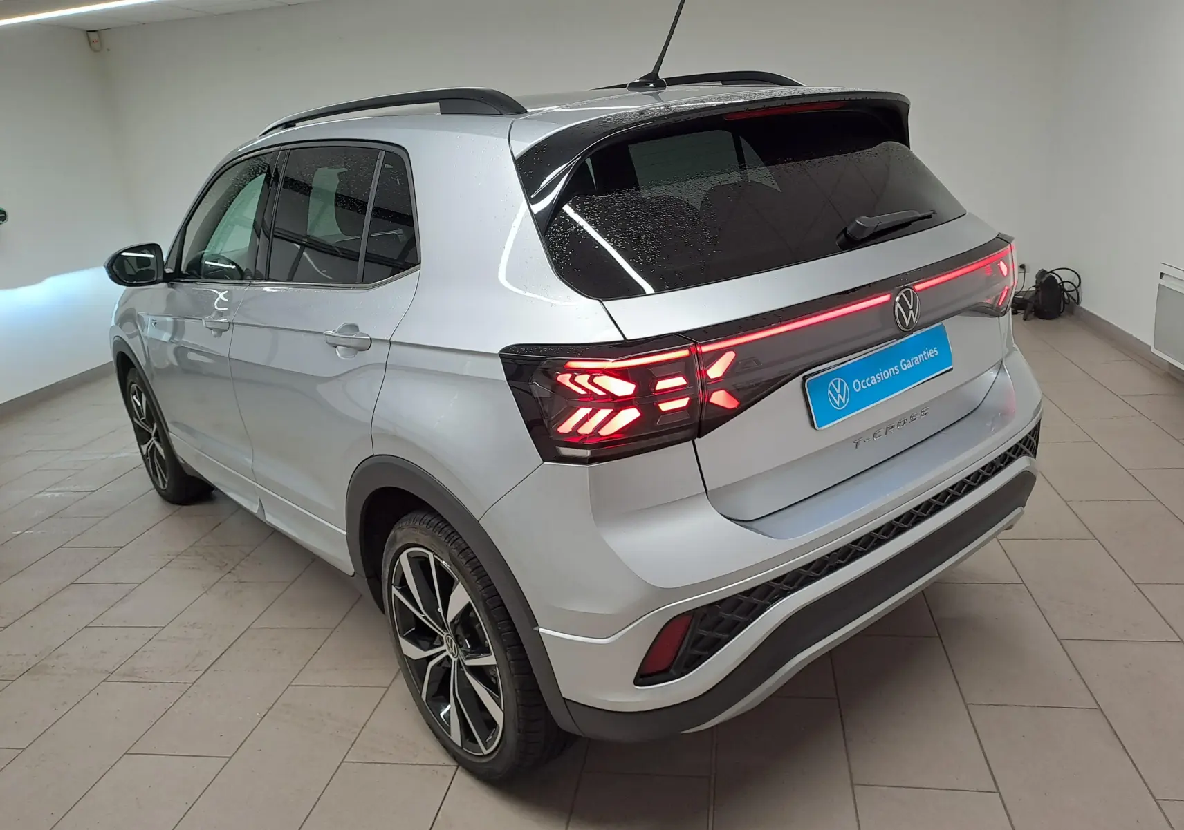 Volkswagen T-Cross 2025 R-Line argent, vue 3/4 arrière droit avec feux arrière allumés en intérieur.