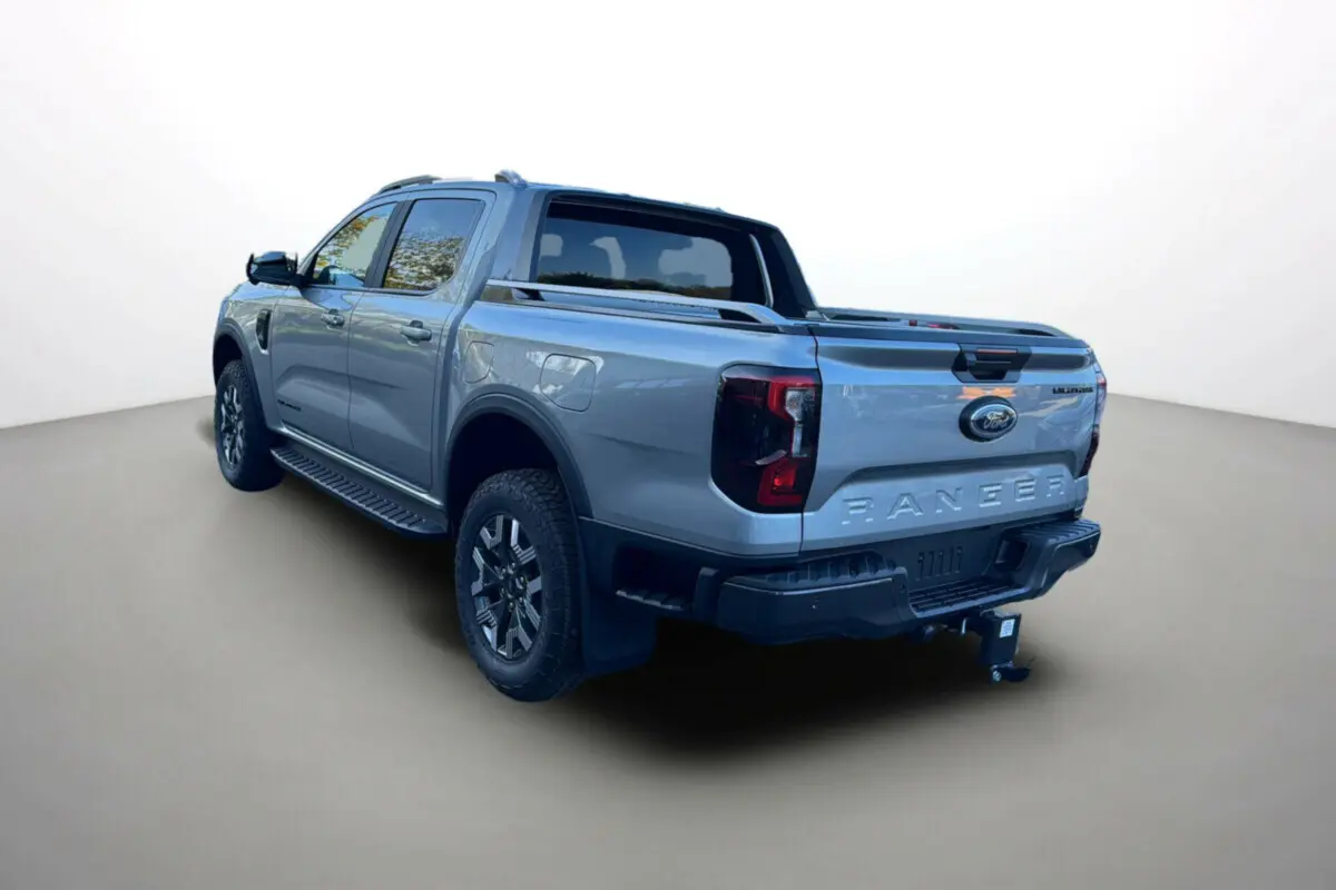 Ford Ranger 2.3 PHEV Wildtrak Plus gris iconic, vue 3/4 arrière droit avec attelage et barres de toit visibles.