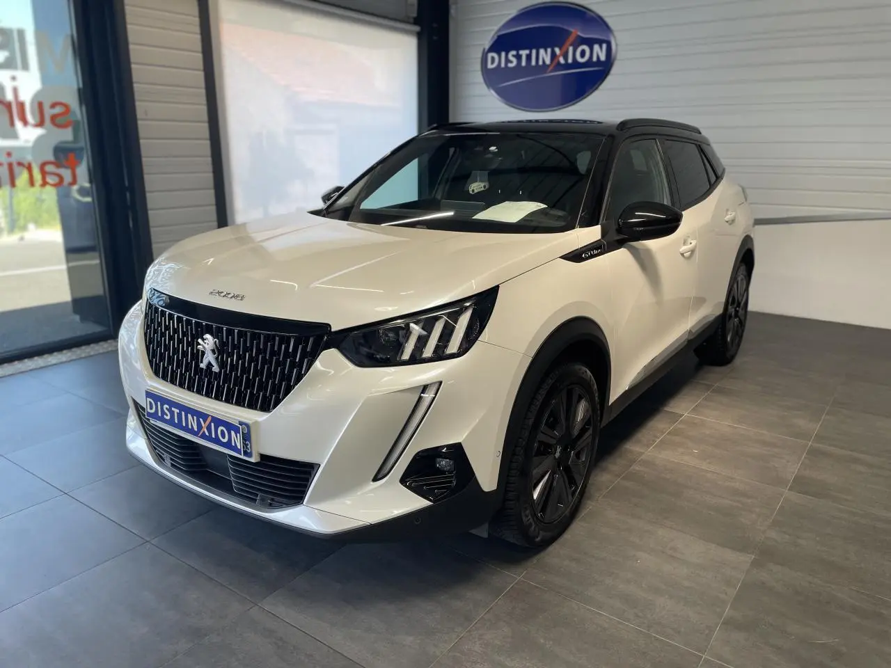Peugeot 2008 blanc vue 3/4 avant droit en intérieur avec calandre noire et jantes foncées.
