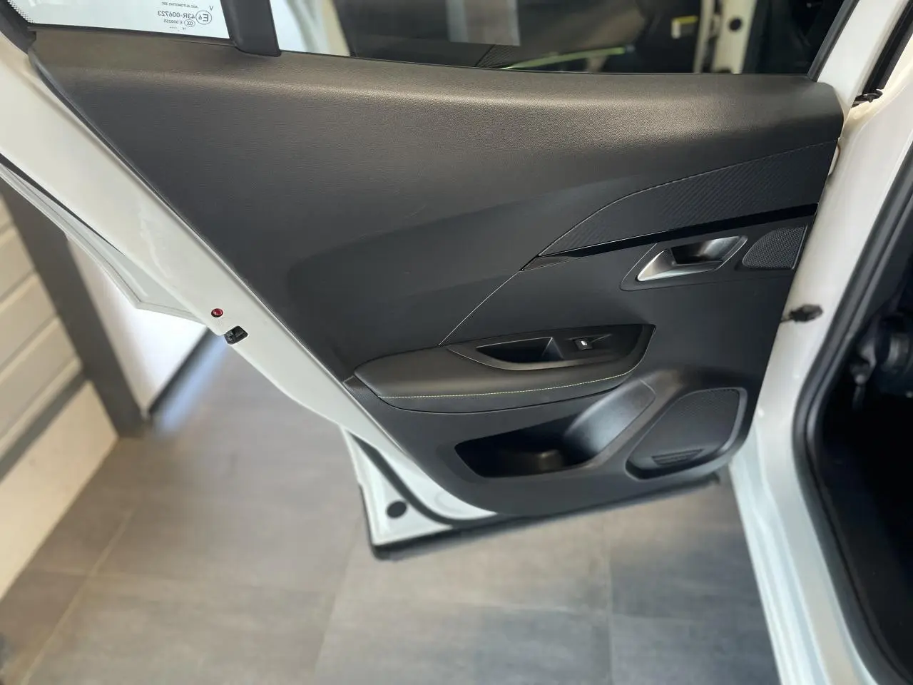 Porte arrière gauche ouverte de la Peugeot 2008 noire, montrant le panneau intérieur noir avec surpiqûres vertes.