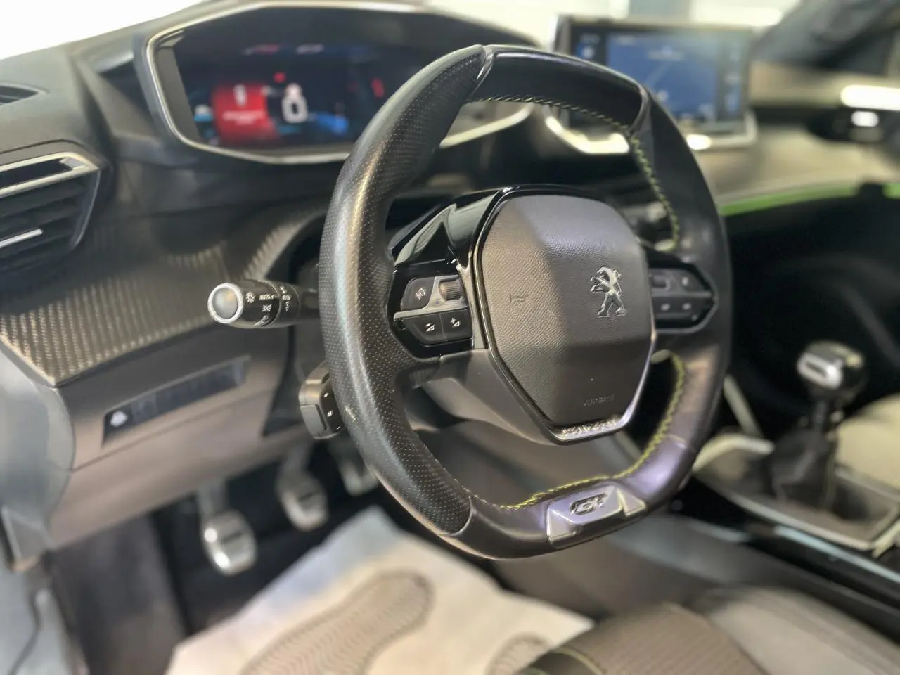 Volant compact cuir noir avec surpiqûres vertes et badge GT Line, tableau de bord et console centrale du Peugeot 2008.