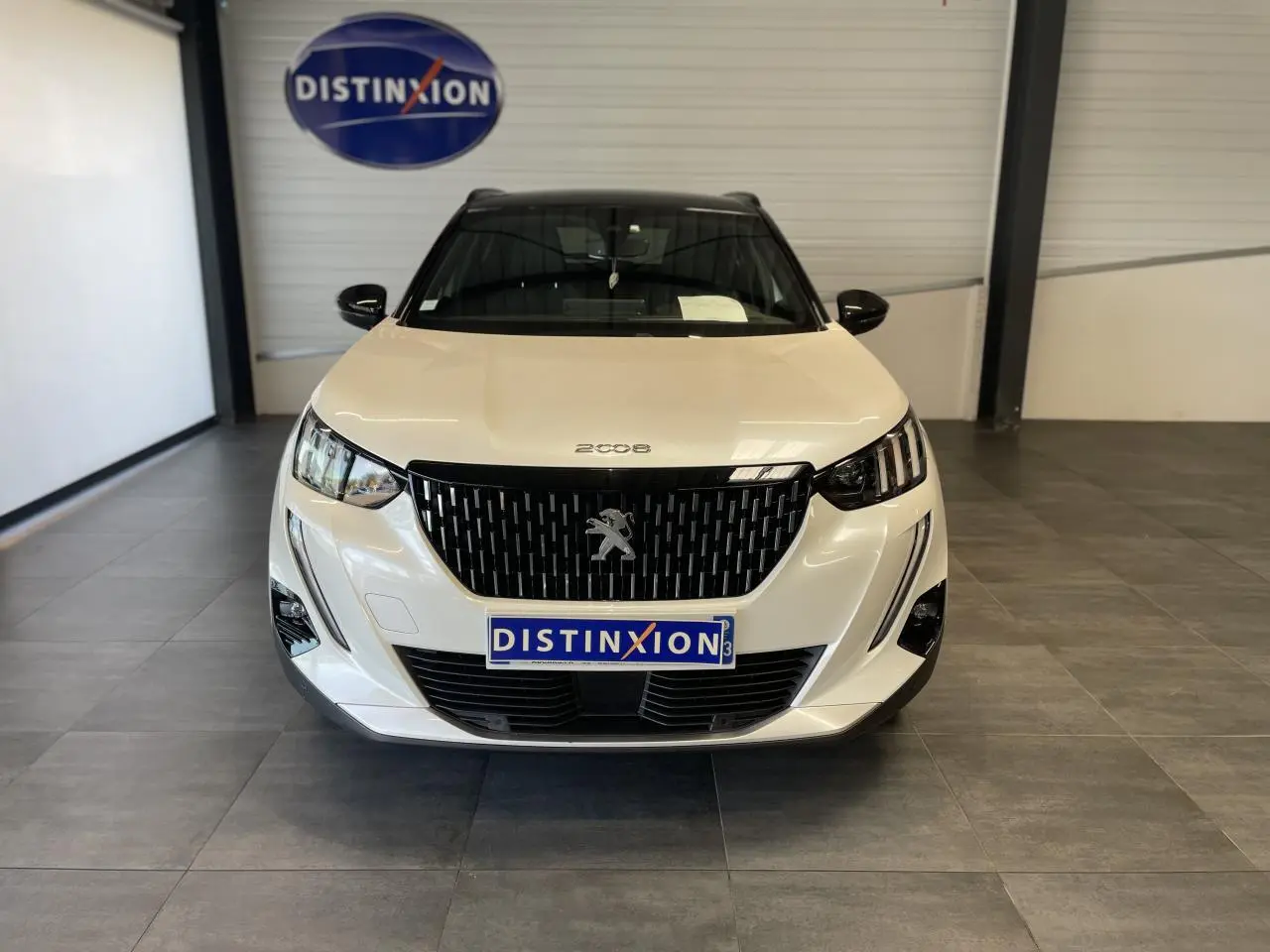 Vue avant d'un Peugeot 2008 blanc avec calandre noire brillante et logo lion au centre, en showroom.
