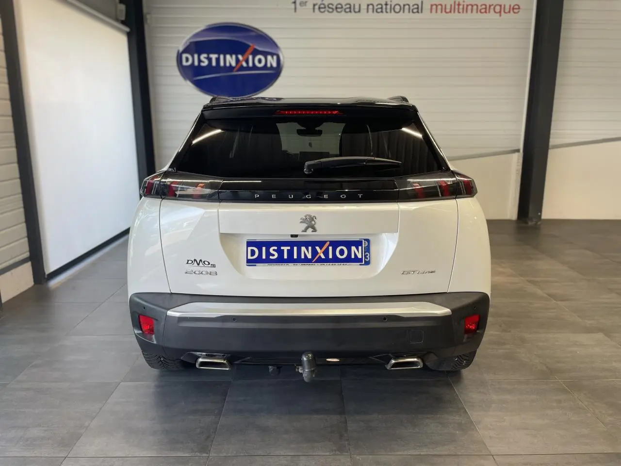 Vue arrière d'un Peugeot 2008 blanc avec toit noir, double sortie d'échappement chromée et attelage visible.