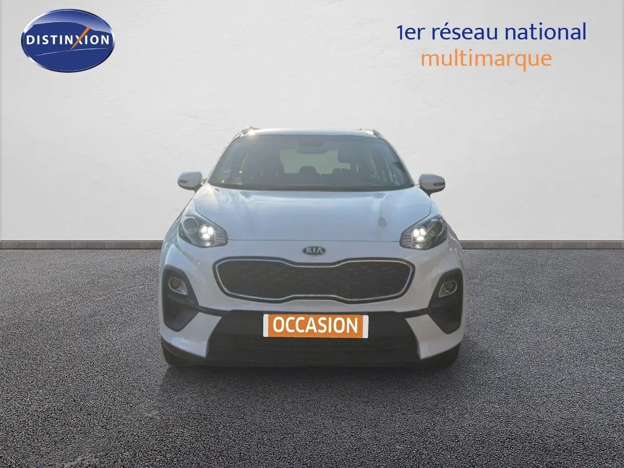 Vue frontale d'un Kia Sportage blanc nacré métal avec phares allumés et plaque "OCCASION" visible.