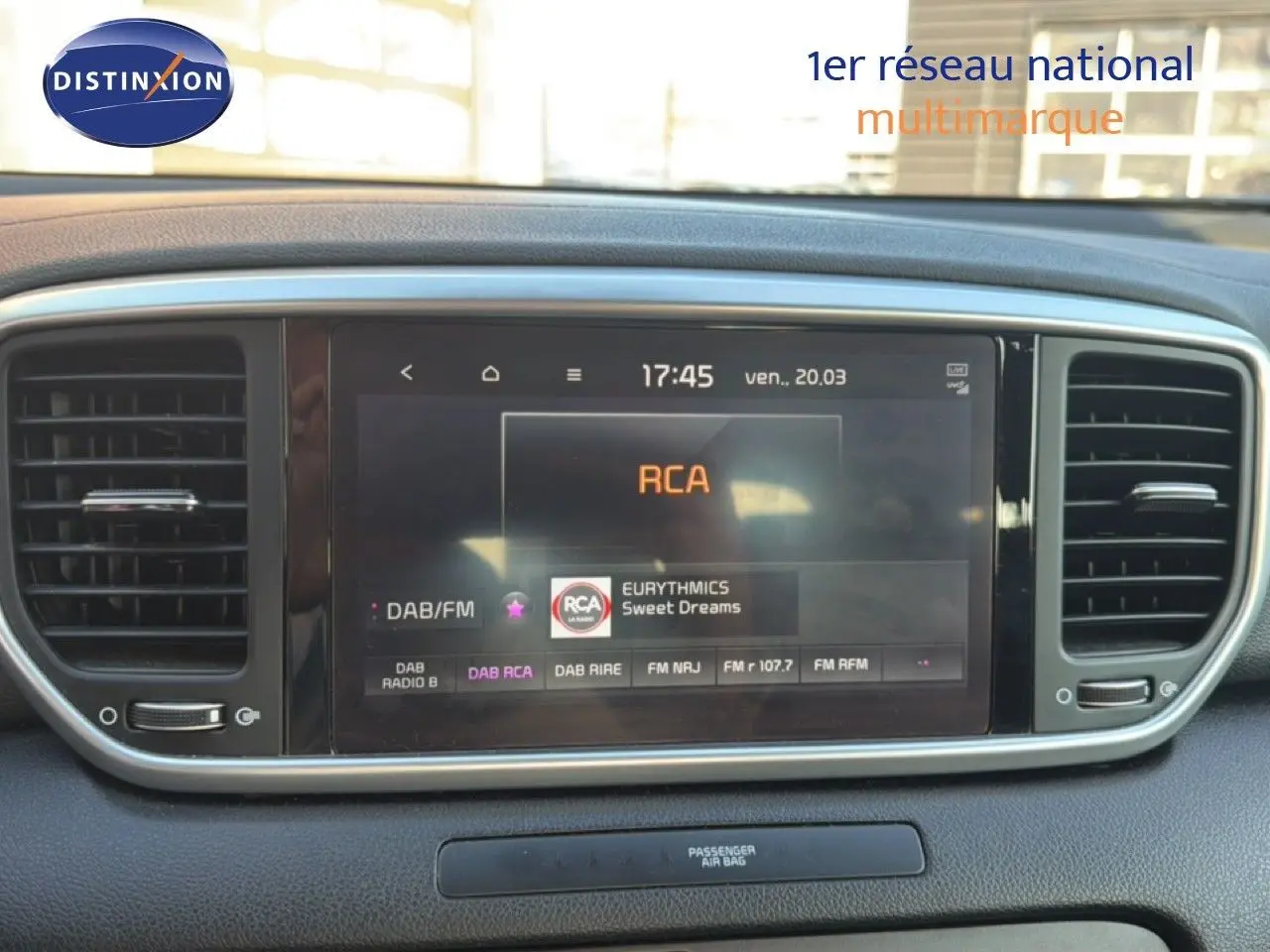 Écran tactile central du tableau de bord du Kia Sportage blanc nacré, affichant la radio RCA en mode DAB/FM.