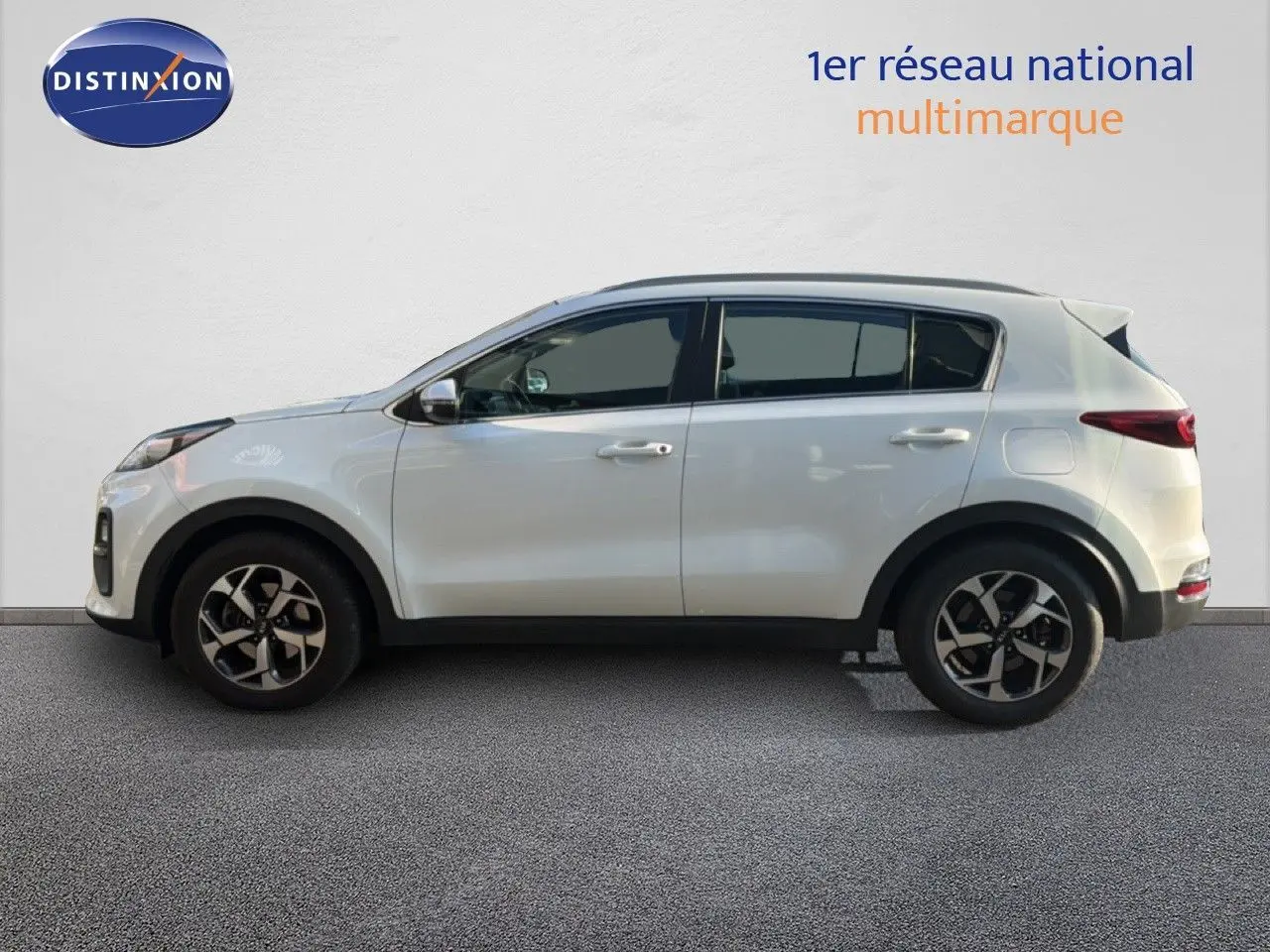 Vue de profil côté gauche d'un Kia Sportage blanc nacré métal, avec jantes bi-ton et vitres teintées.
