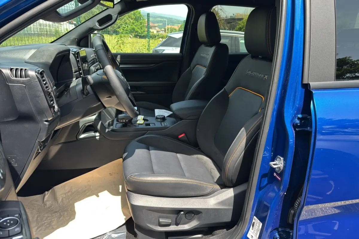 Vue intérieure côté conducteur du Ford Ranger 2026 bleu lightning, sièges Wildtrak X avec surpiqûres orange et tableau de bord moderne.
