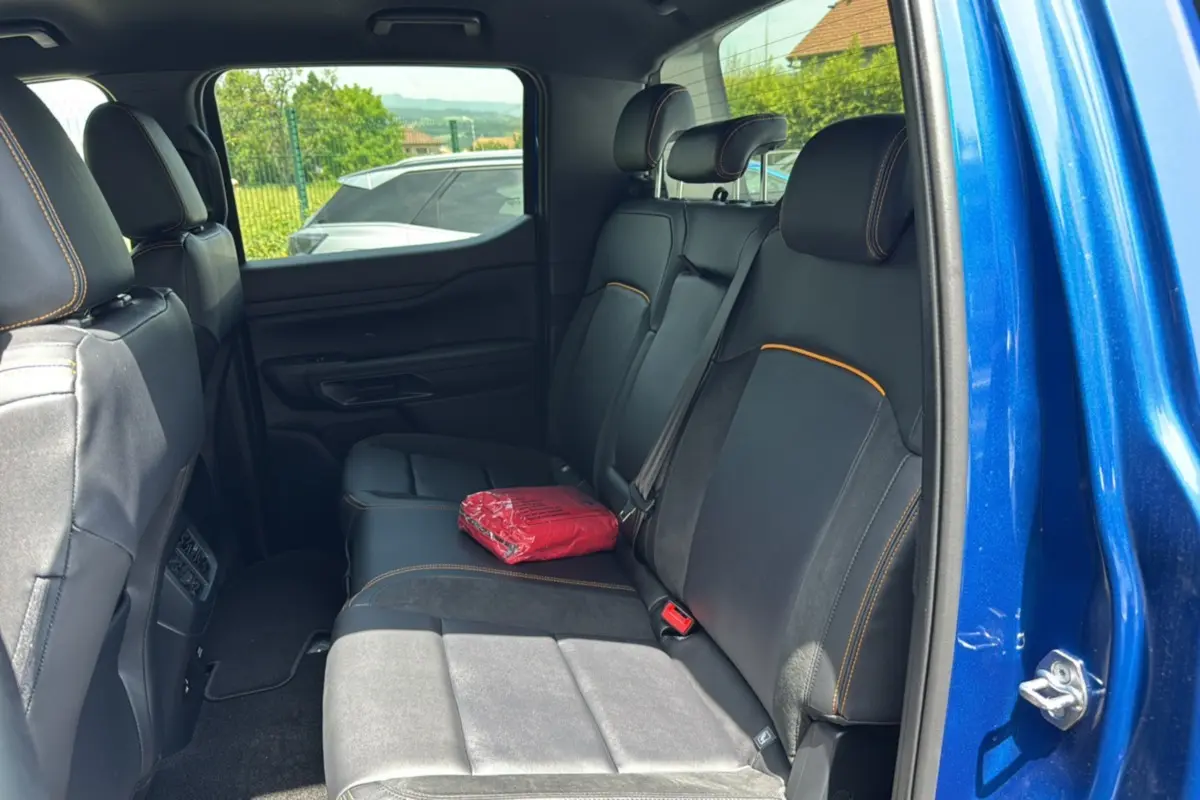 Vue intérieure arrière côté droit du Ford Ranger 2026 bleu lightning, sièges noirs avec surpiqûres orange et rideau coulissant.