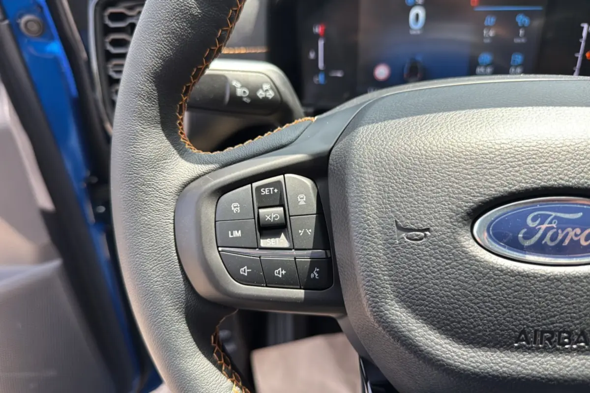 Gros plan sur le volant cuir noir avec surpiqûres orange du Ford Ranger Bleu Lightning, boutons multifonctions visibles.