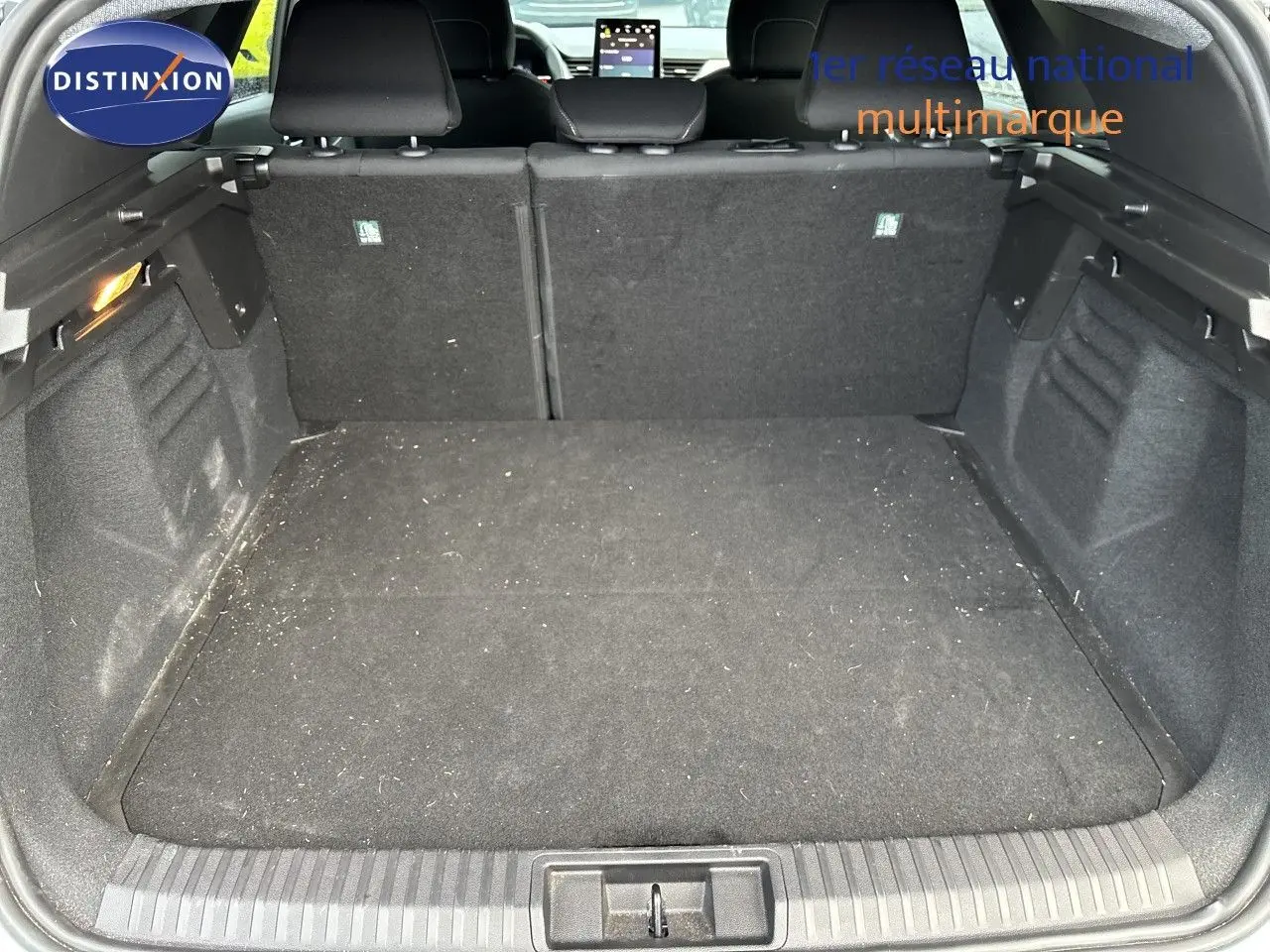 Vue intérieure du coffre spacieux et noir d’un Renault Symbioz blanc nacré, avec sièges arrière et écran tactile visibles.