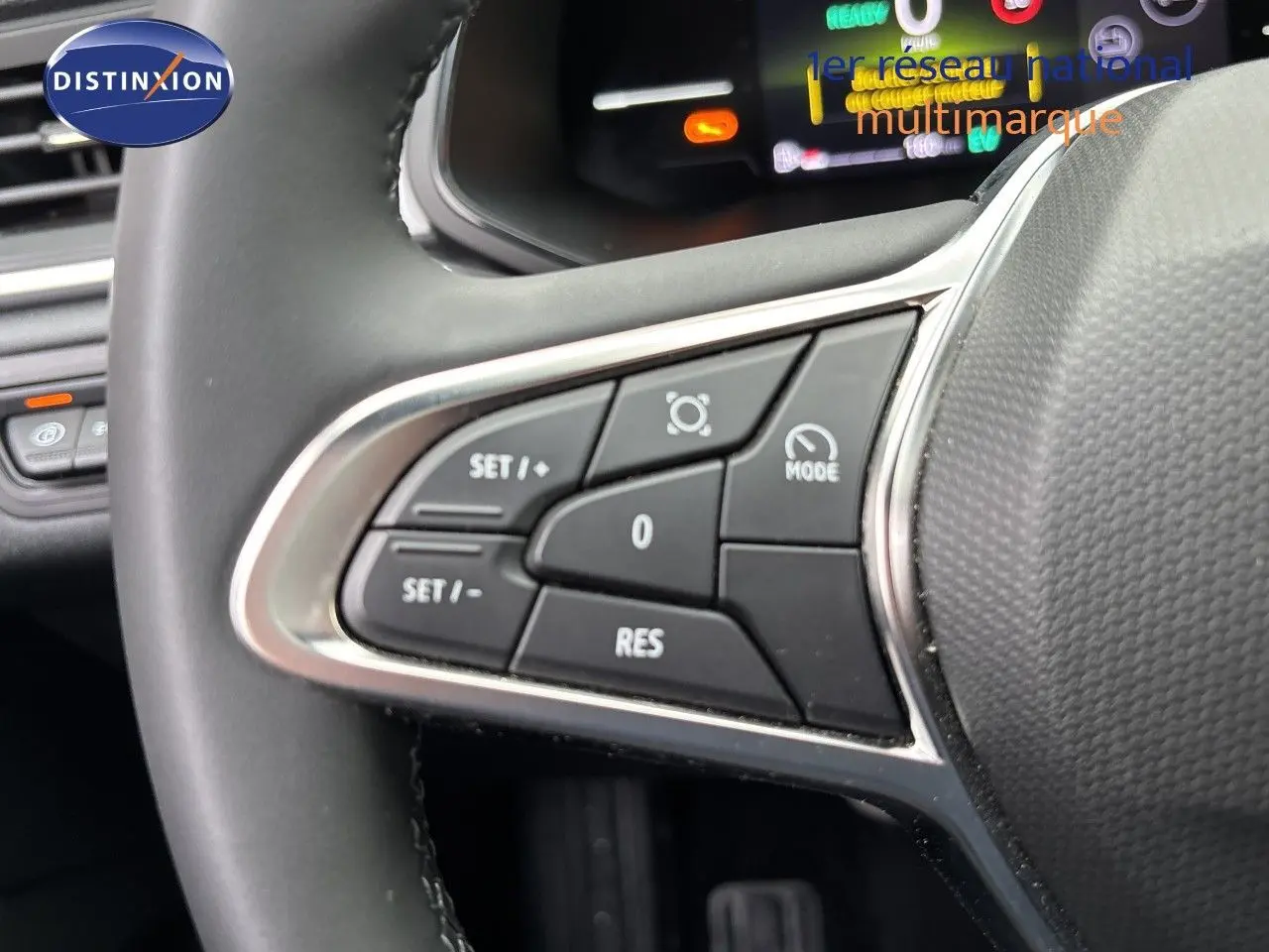 Gros plan sur les commandes de régulateur de vitesse au volant d’un Renault Symbioz blanc nacré, tableau de bord numérique en arrière-plan.