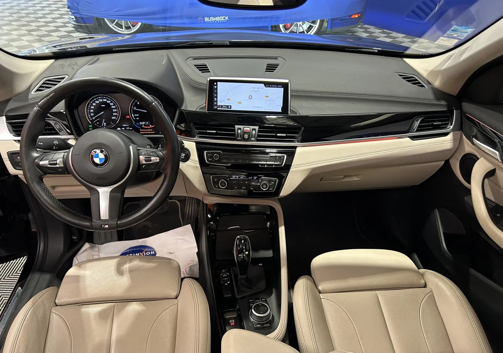 Vue intérieure avant du BMW X1 2019 avec sièges cuir beige, tableau de bord noir et écran central GPS.