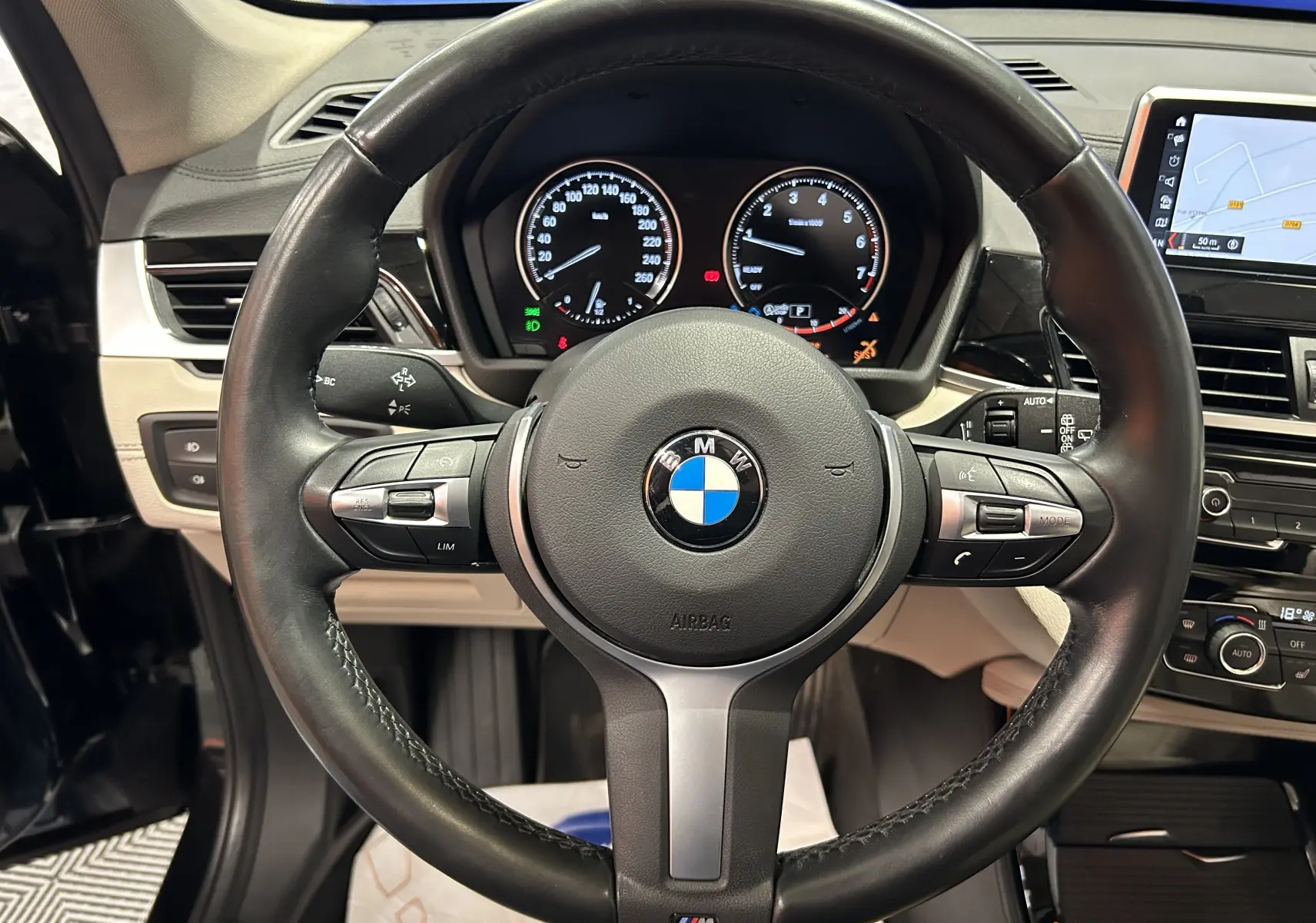 Vue rapprochée du volant cuir noir BMW X1 2019 avec tableau de bord et écran GPS intégré visible.