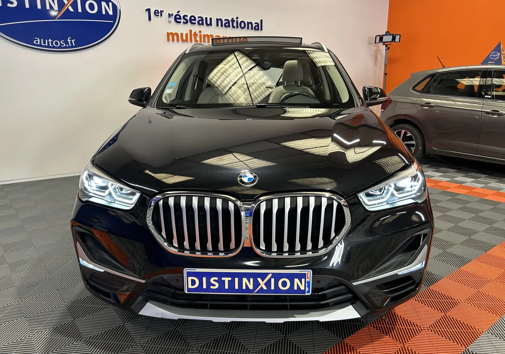Vue avant d'un BMW X1 noir 2019 avec calandre chromée et phares LED allumés en intérieur showroom.