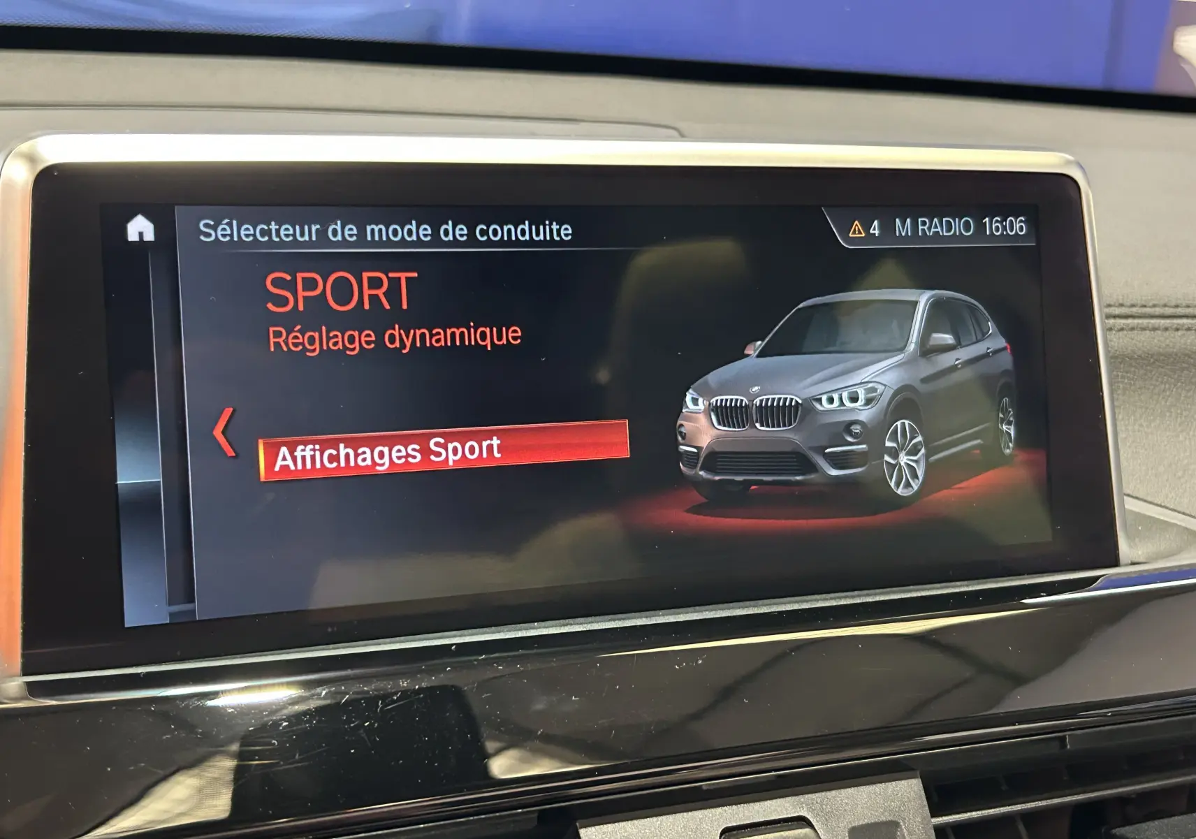 Écran central affichant le mode de conduite Sport avec une image 3/4 avant d'un BMW X1 noir.