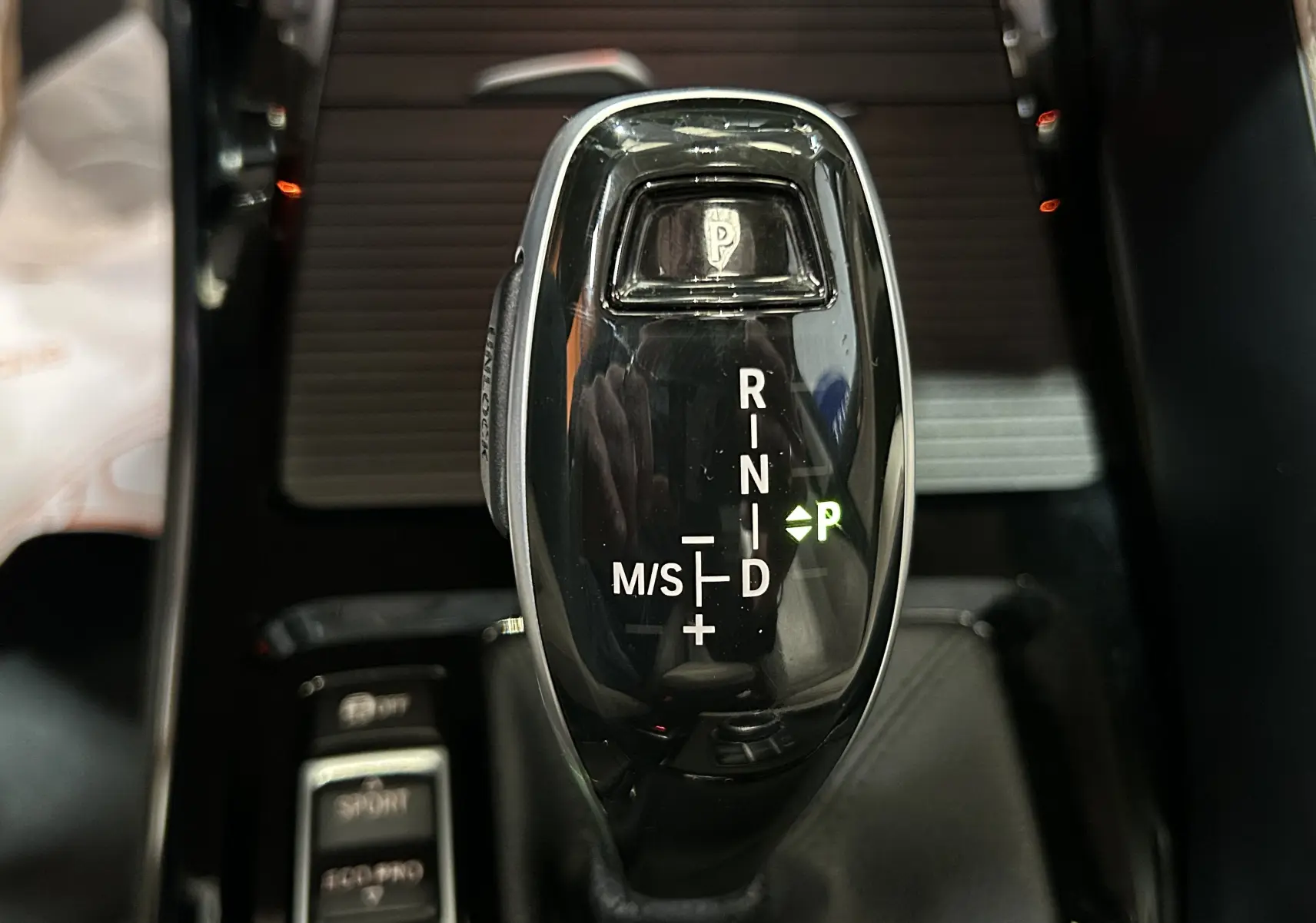 Gros plan sur le levier de vitesse automatique noir brillant du BMW X1 sDrive18iA, avec indication mode parking verte.