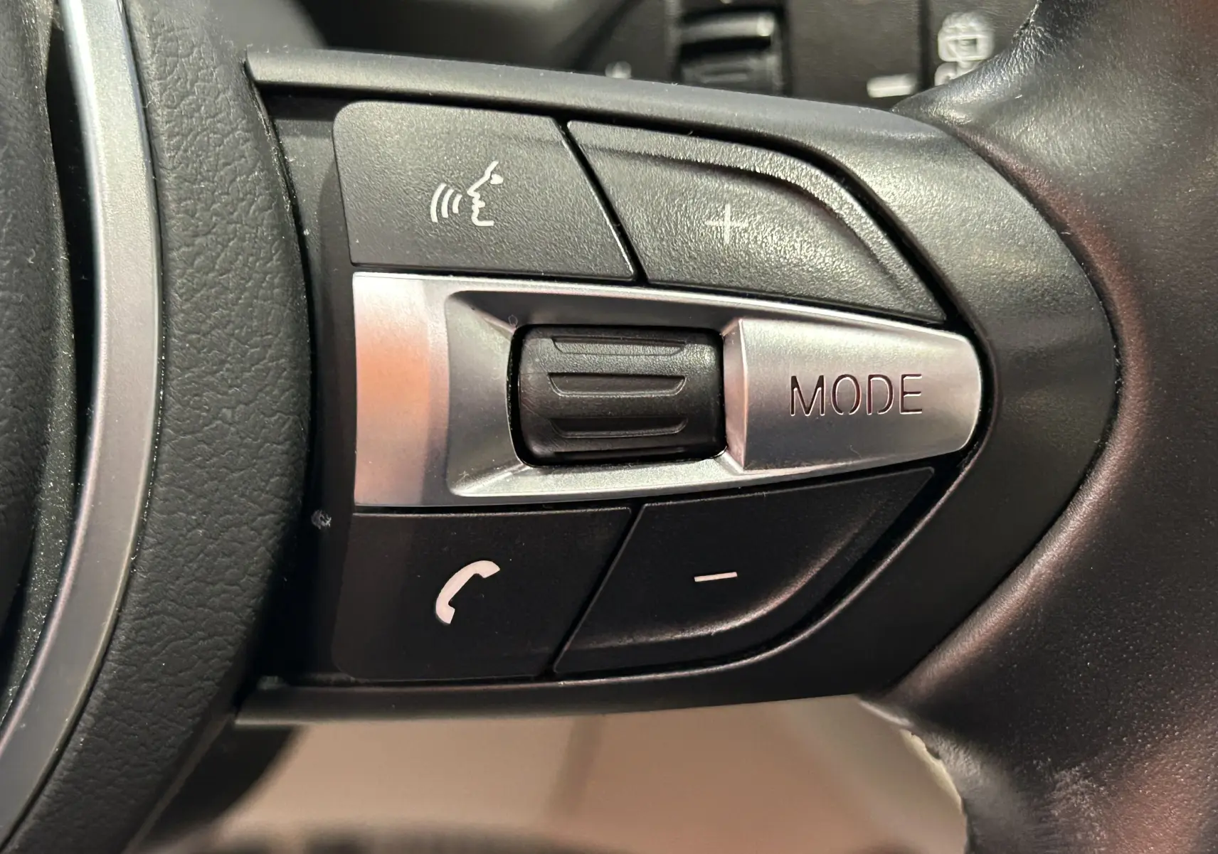 Gros plan sur les commandes multifonctions en plastique noir et argent du volant d’un BMW X1 noir de 2019.