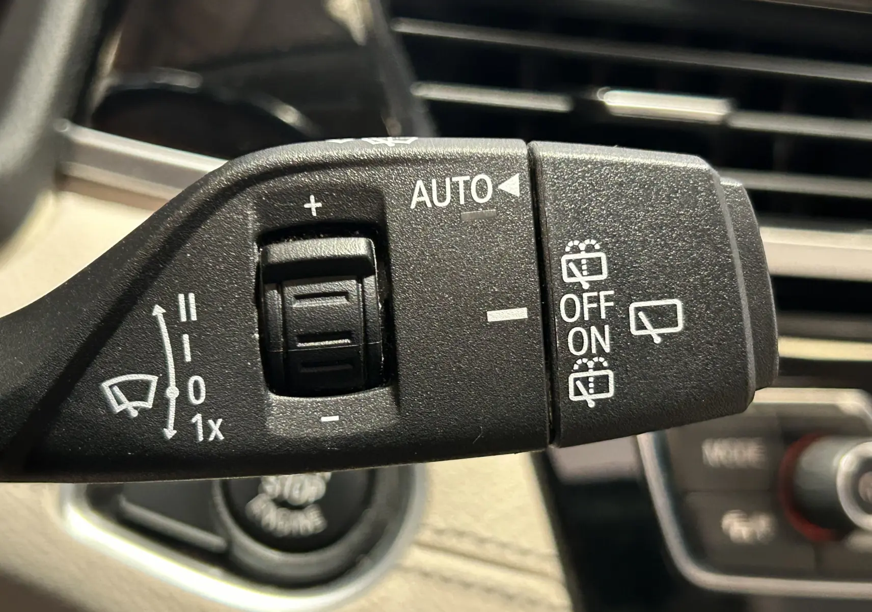 Gros plan sur la commande des essuie-glaces d’un BMW X1 noir, avec réglage automatique et options de lavage visibles.