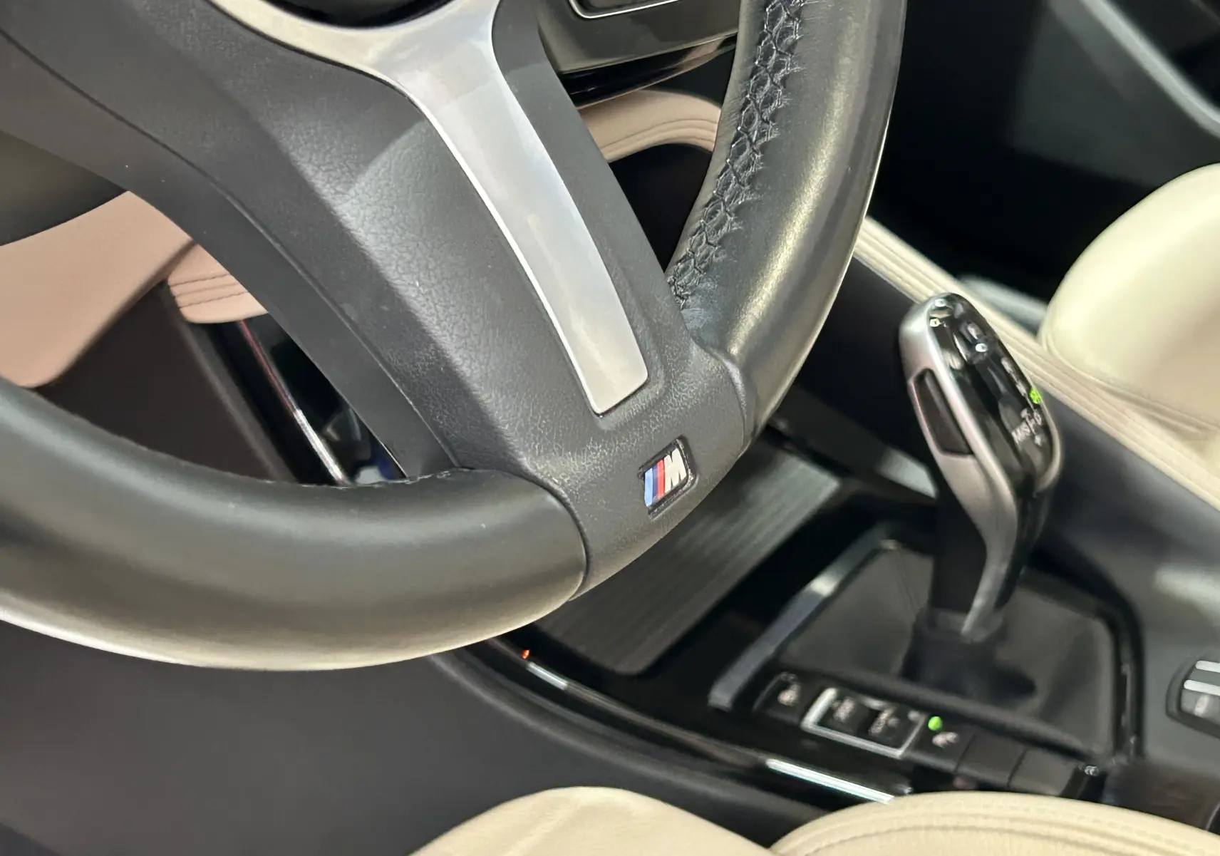 Gros plan sur le volant M en cuir noir et levier de vitesse automatique dans l’habitacle beige du BMW X1 noir.