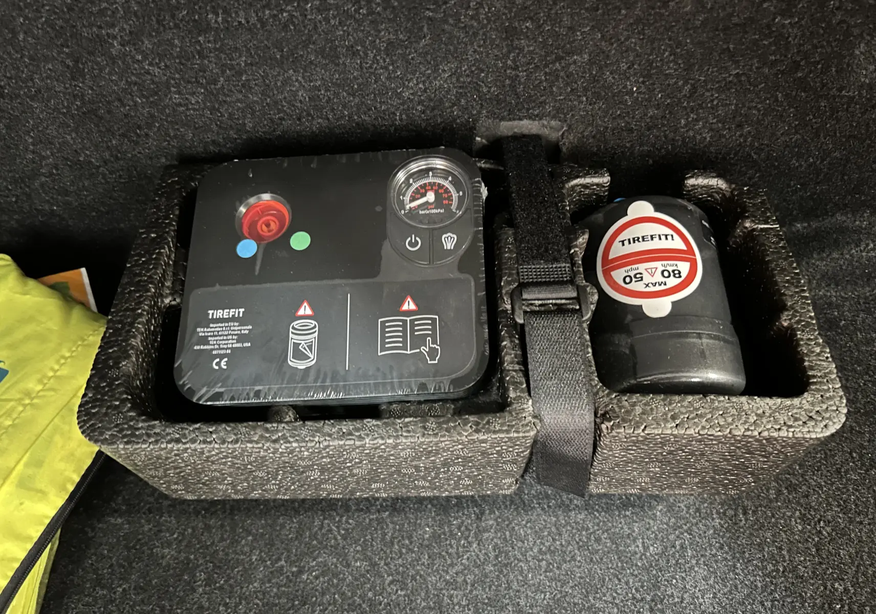 Gros plan sur le compresseur et le flacon de produit Tirefit dans le coffre du BMW X1 noir, version sDrive18iA 2019.