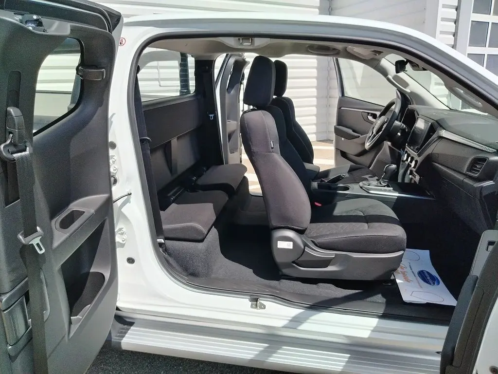 Vue latérale intérieure du pick-up Isuzu D-MAX blanc 2026, montrant les sièges avant et arrière en tissu noir.