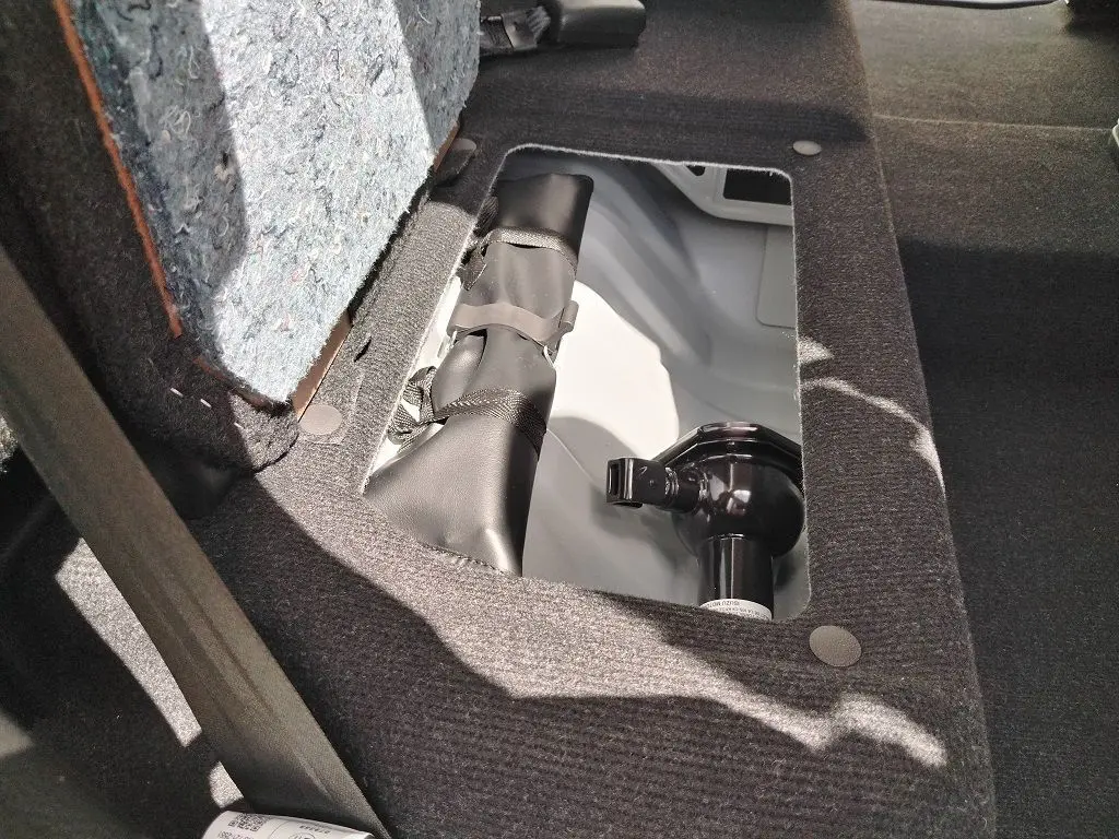 Détail du compartiment de rangement sous le siège arrière du pick-up Isuzu D-MAX blanc, montrant un crochet d'attelage.