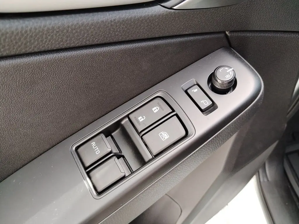 Gros plan sur les commandes de lève-vitres et réglage des rétroviseurs côté conducteur d'un Isuzu D-MAX blanc.