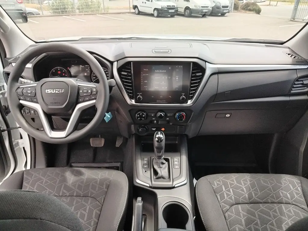Vue intérieure avant de l'Isuzu D-MAX 2026 avec tableau de bord noir et volant multifonction.