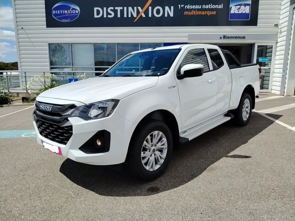 Vue 3/4 avant d'un Isuzu D-MAX blanc avec arceau et couvre benne roulant, stationné devant un bâtiment Distinxion.