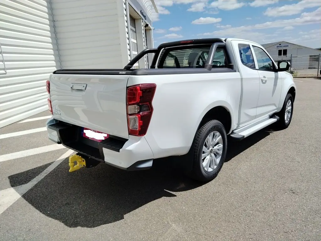 Vue 3/4 arrière droite d’un Isuzu D-MAX blanc avec arceau noir et volet couvre benne roulant, stationné en extérieur.