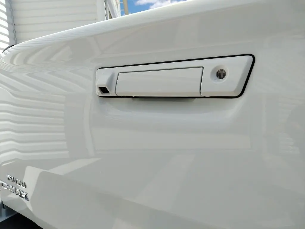 Gros plan sur la poignée blanche de la benne du pick-up Isuzu D-MAX 2026 avec logo visible en bas à gauche.