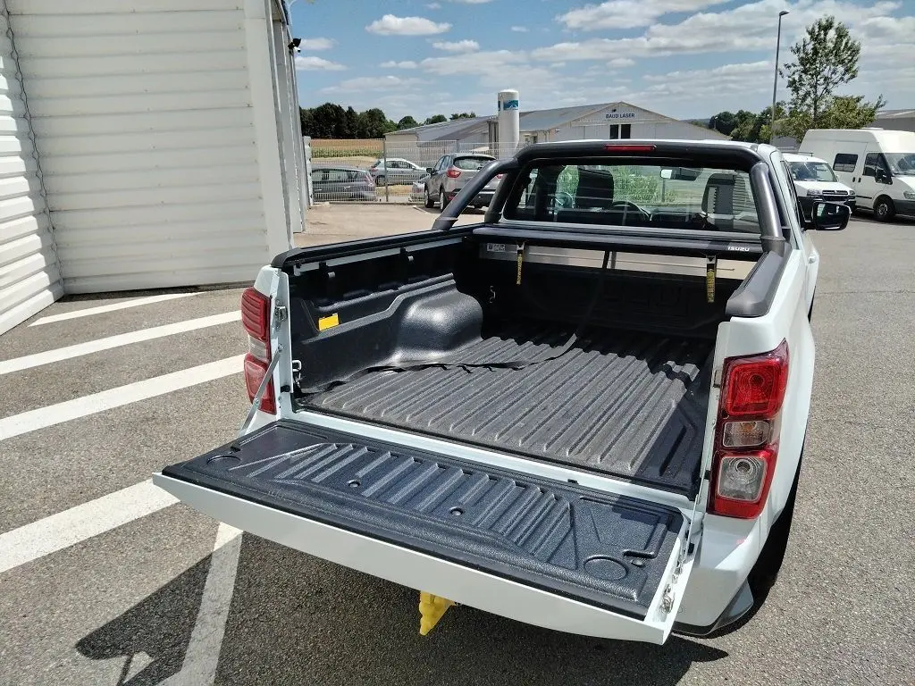 Vue arrière en 3/4 du pick-up Isuzu D-MAX blanc avec benne ouverte, arceau et volet couvre benne roulant visible.