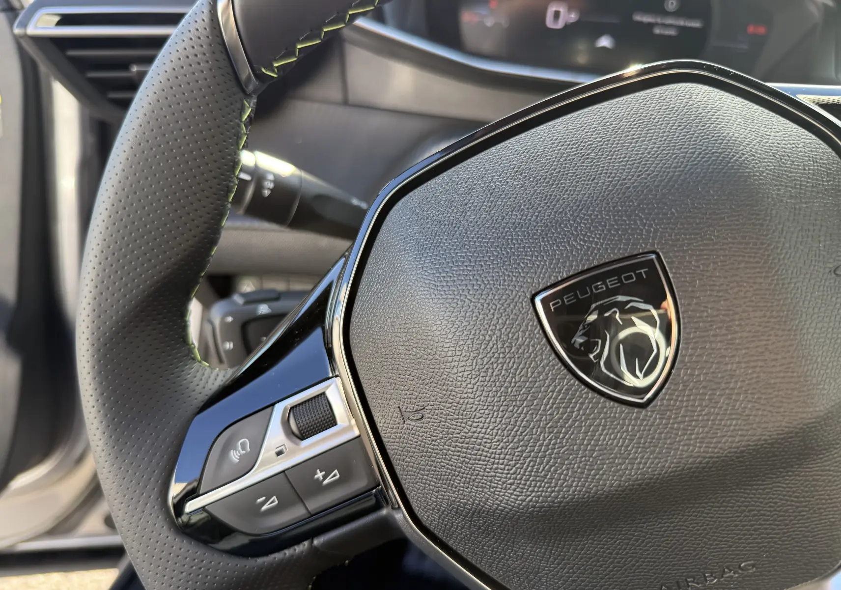 Gros plan sur le volant noir texturé du Peugeot 2008 Hybrid 145 GT, avec commandes intégrées et logo lion central.
