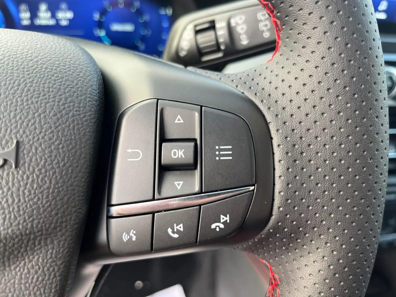 Gros plan sur les commandes du volant perforé avec surpiqûres rouges du Ford Kuga 1.5 EcoBoost 150 ST-Line 2022.