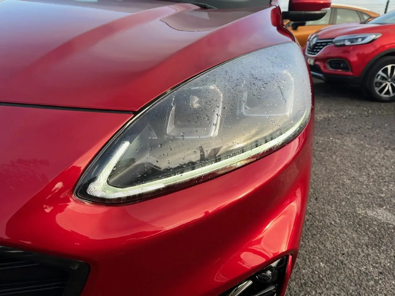 Gros plan sur le phare avant gauche du Ford Kuga rouge Lucifer 2022 avec gouttes d'eau et calandre partielle visible.