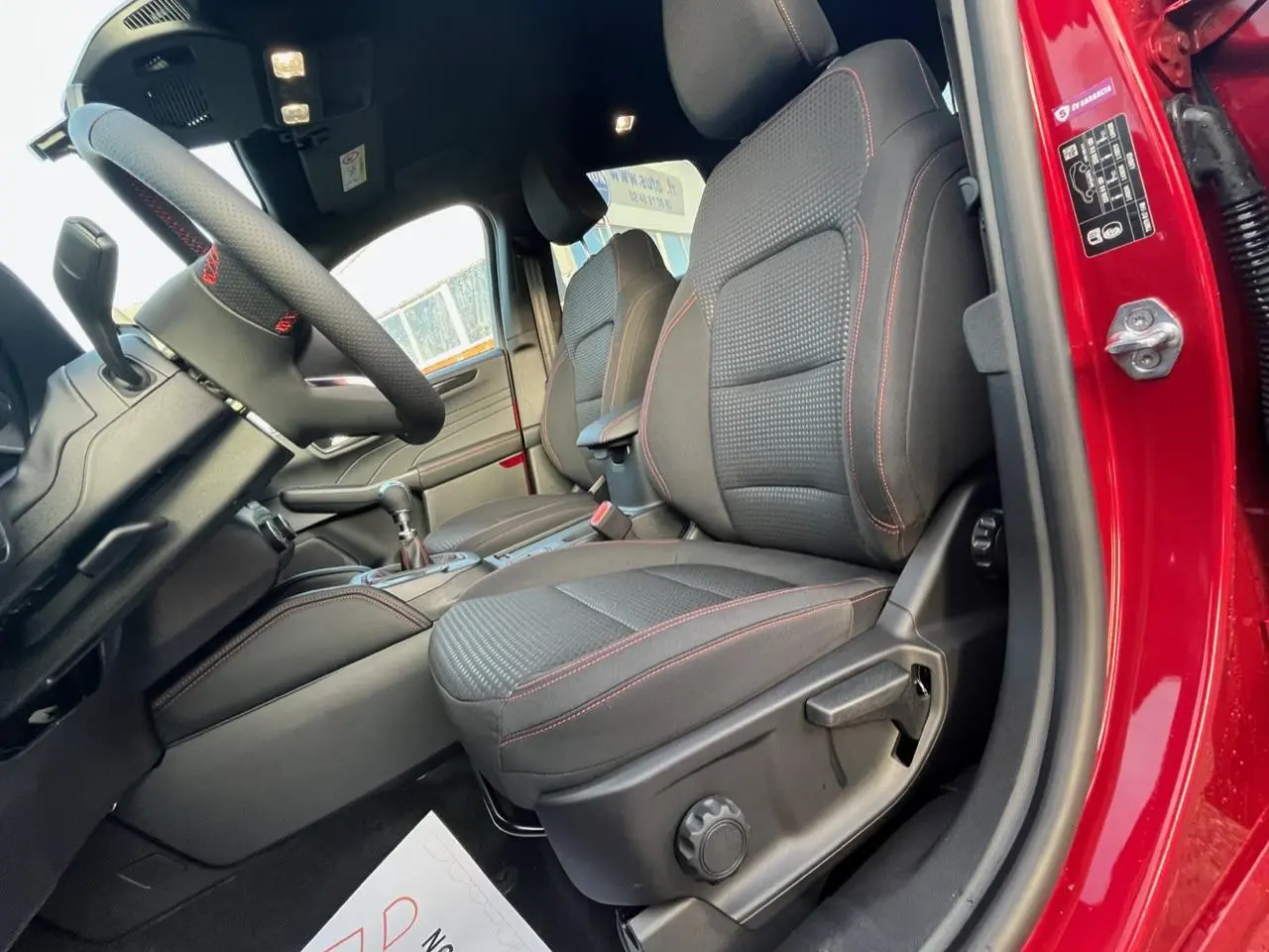 Vue intérieure côté conducteur du Ford Kuga rouge Lucifer 2022, sièges tissu noirs avec surpiqûres rouges et volant sport.