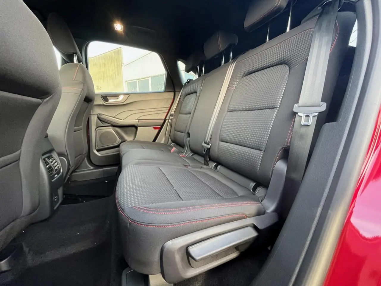 Vue latérale intérieure montrant la banquette arrière noire avec surpiqûres rouges du Ford Kuga rouge Lucifer 2022.