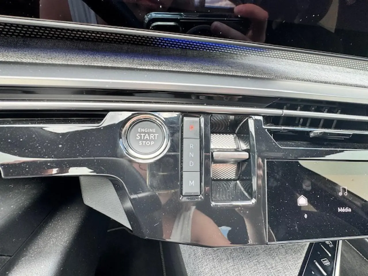 Gros plan sur la console centrale noire brillante du Peugeot 3008 II hybride 2024, avec bouton start/stop et sélecteur de vitesses.