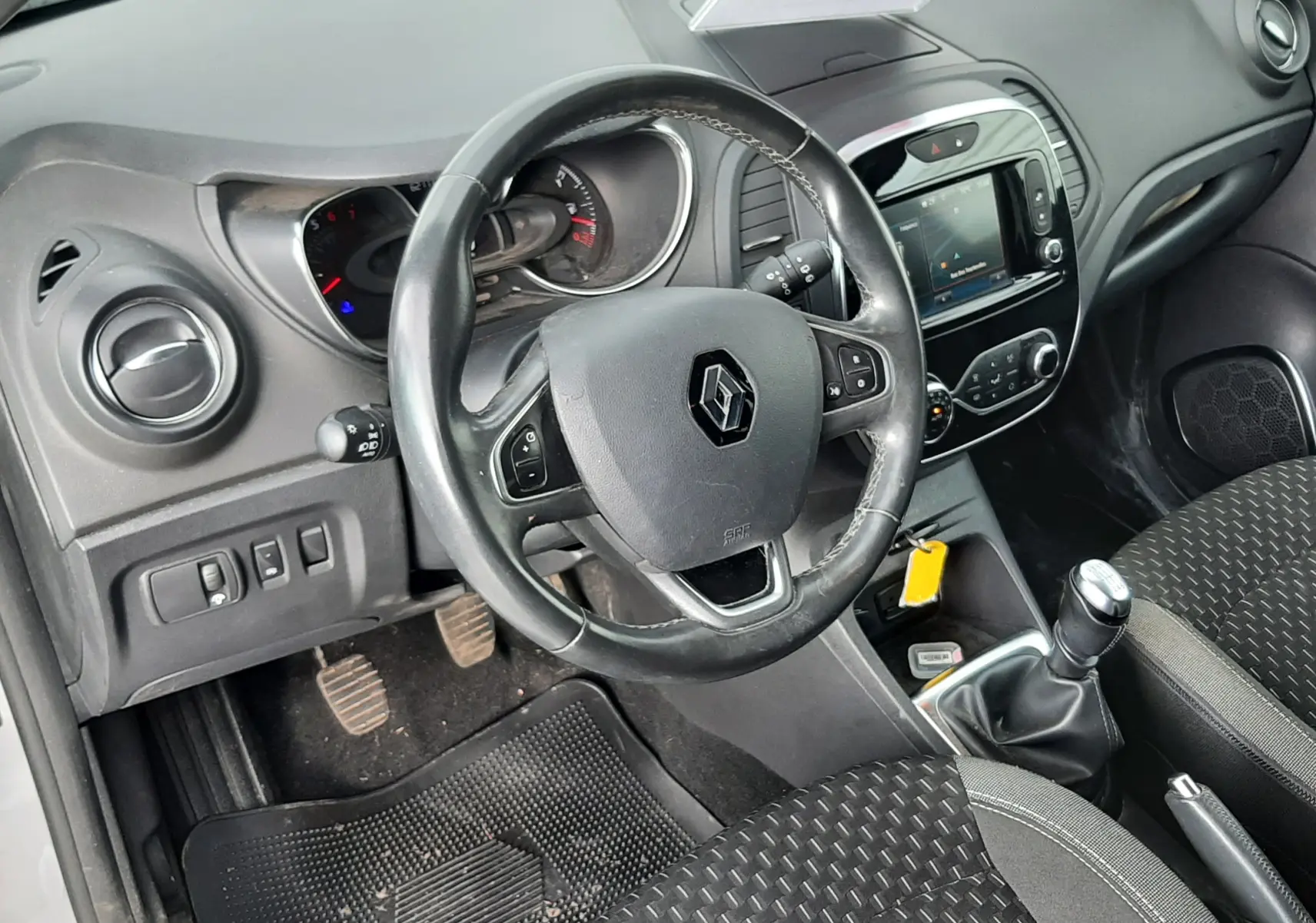 Vue intérieure côté conducteur du tableau de bord et volant noir d'un Renault Captur gris toit noir, avec levier de vitesse manuel.