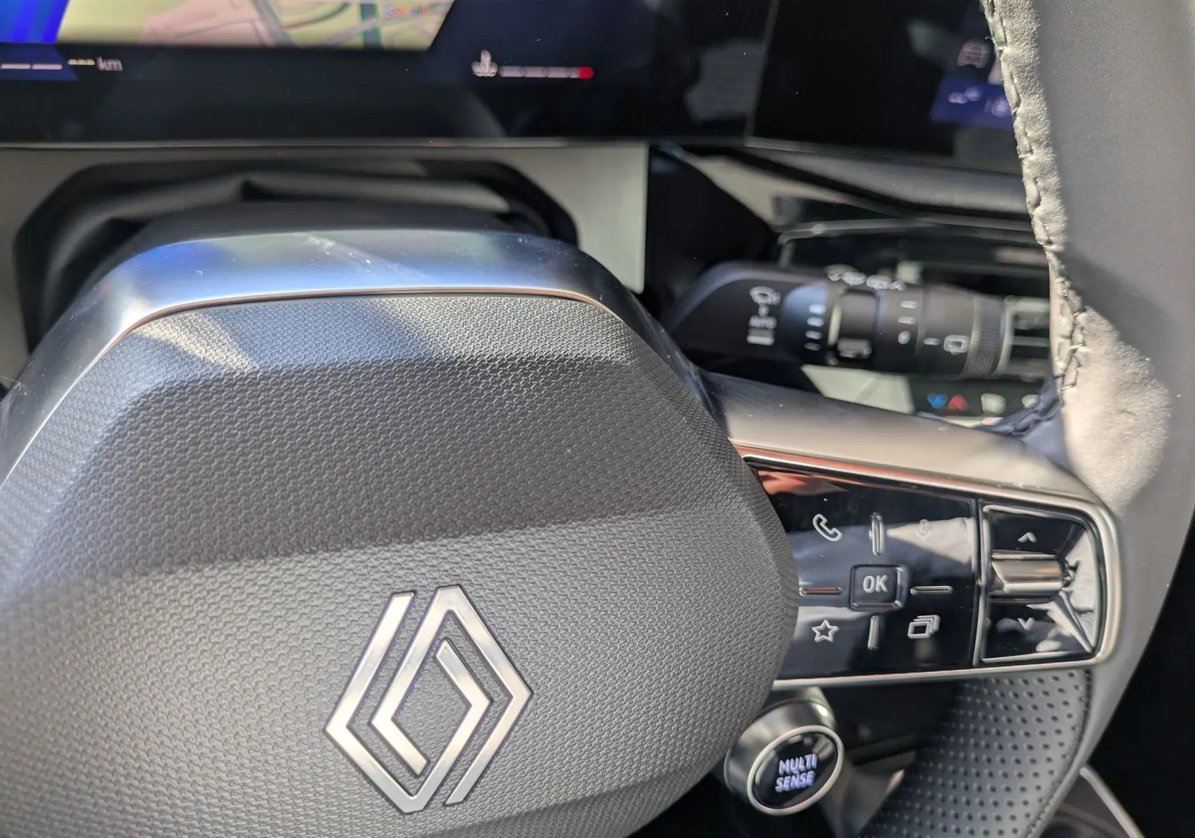 Gros plan sur le volant noir texturé de la Renault Clio VI TCe 115ch Techno, avec commandes intégrées et logo central argenté.
