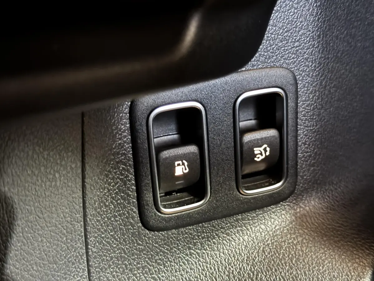 Gros plan sur les boutons d'ouverture de trappe à carburant et coffre dans un Mercedes GLA 250 e Business Line gris foncé.
