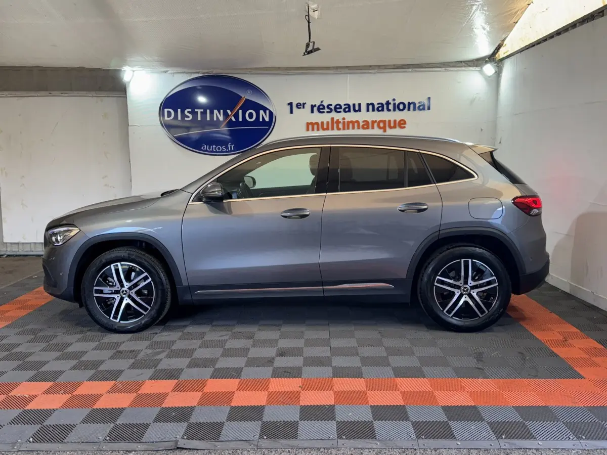 Vue de profil côté gauche d'un Mercedes GLA 250 e Business Line gris foncé, stationné en intérieur sur sol à damiers noir et orange.