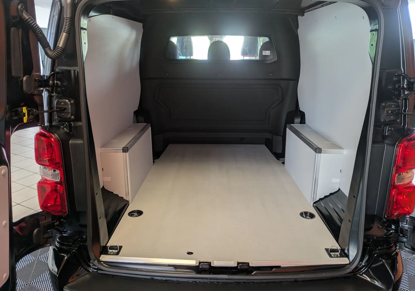 Vue arrière du Citroën Jumpy Cabine Approfondie noir, montrant l’espace de chargement avec plancher bois et coffrages latéraux blancs.