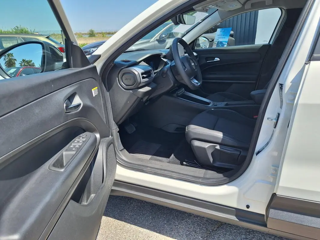 Intérieur côté conducteur du Jeep Avenger blanc 2025, avec tableau de bord et sièges noirs visibles depuis la portière ouverte.
