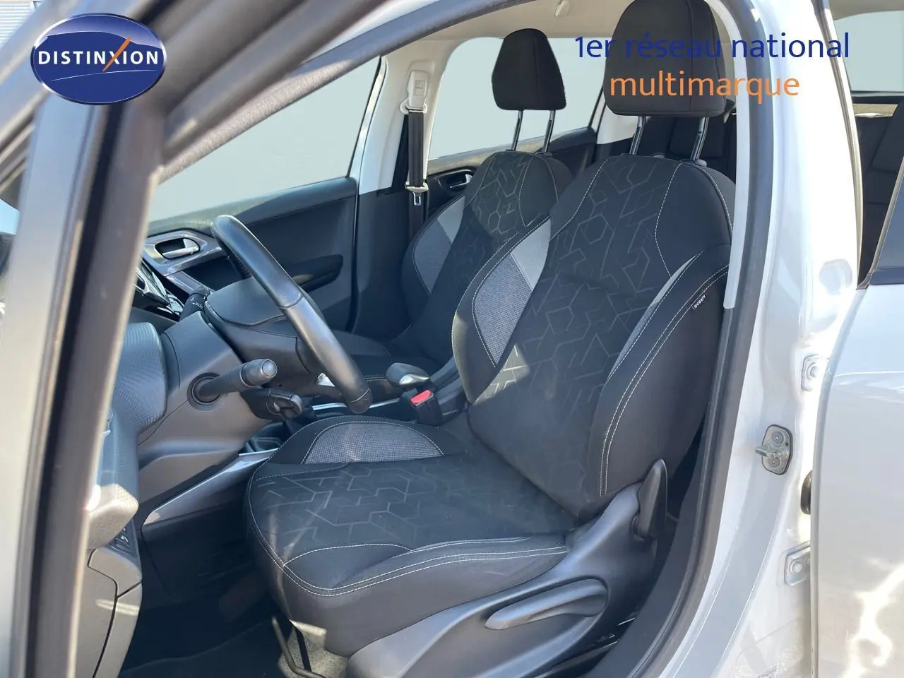 Vue intérieure côté conducteur d'une Peugeot 2008 blanche de 2017, sièges tissu gris noir avec motifs géométriques.